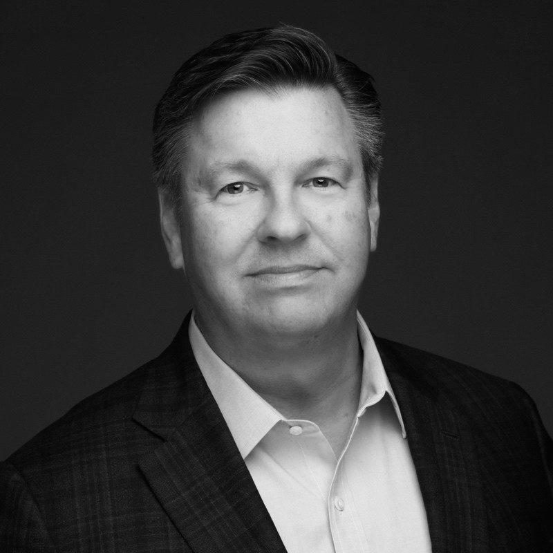 Portrait of a man in a suit, looking confidently at the camera against a dark background.